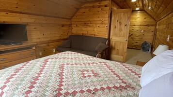 Een knus slaapkamer op zolder met houten wanden, een bed met een bedsprei met patroon, een bureau en een stoel.