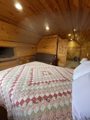 Um quarto de sótão aconchegante com paredes de madeira, uma cama com colcha estampada, uma escrivaninha e uma cadeira.