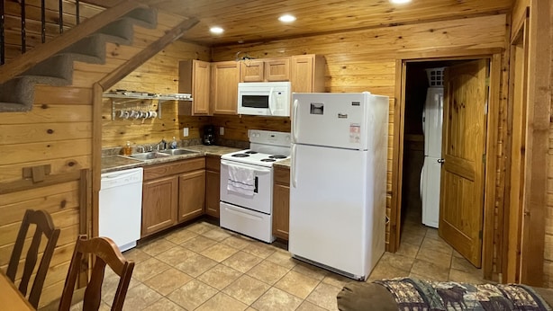 Une cuisine chaleureuse aux murs en bois, un coin repas avec une table et des chaises, et un escalier menant à un autre niveau.