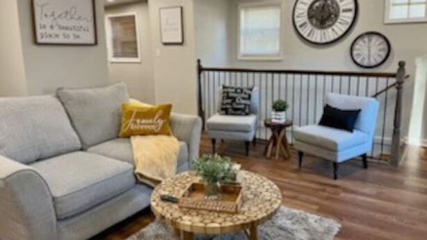 A living room with a grey sofa, a round coffee table, a blue armchair, and a staircase with a railing. - Quaint home in a quiet neighborhood!! Near airport! (East Point)