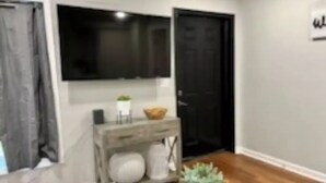 A modern living room with a wooden floor, a grey sofa, a coffee table, and a TV mounted on the wall. - Quaint home in a quiet neighborhood!! Near airport! (East Point)