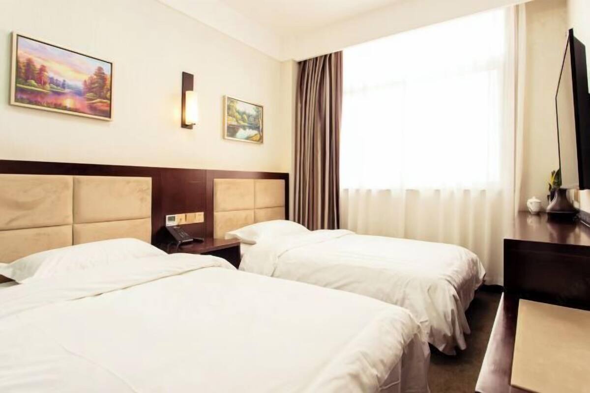 A hotel room with two beds, a desk, a chair, a TV, and a window with curtains.