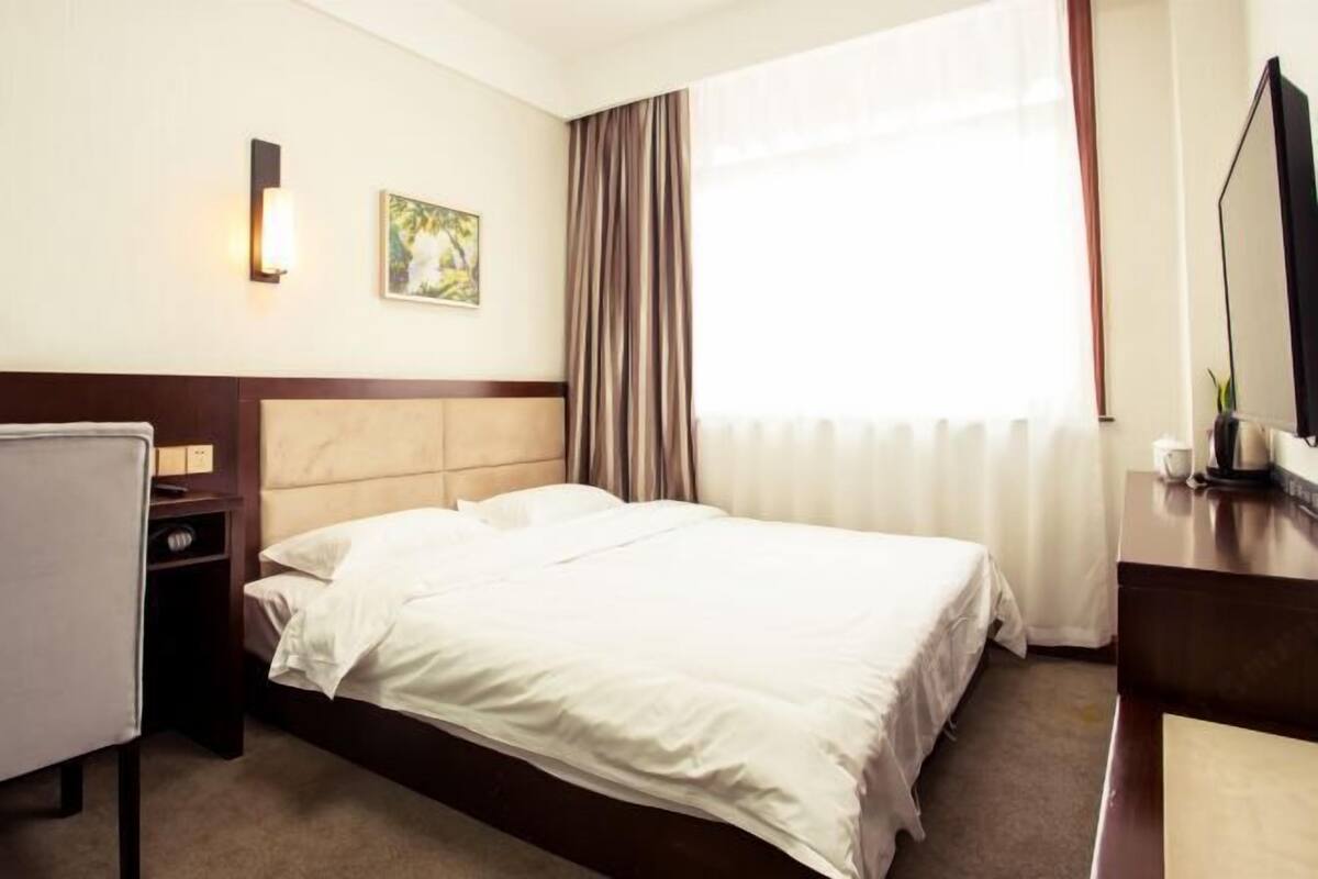 A hotel room with a bed, a desk, a chair, a TV, and a window with curtains.