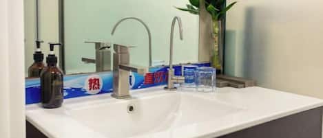 A bathroom with a white sink, two faucets, a mirror, and a plant.