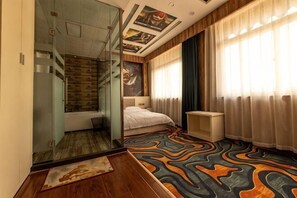 A bedroom with a bed, a glass partition, a desk, and a window with curtains.