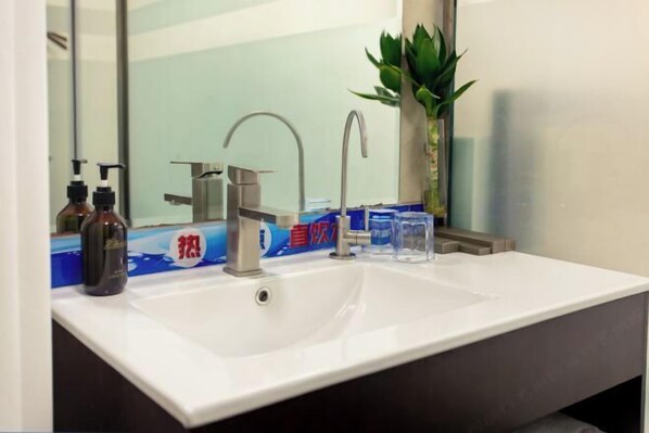 Une salle de bain avec un lavabo blanc, un miroir, un robinet et une plante.