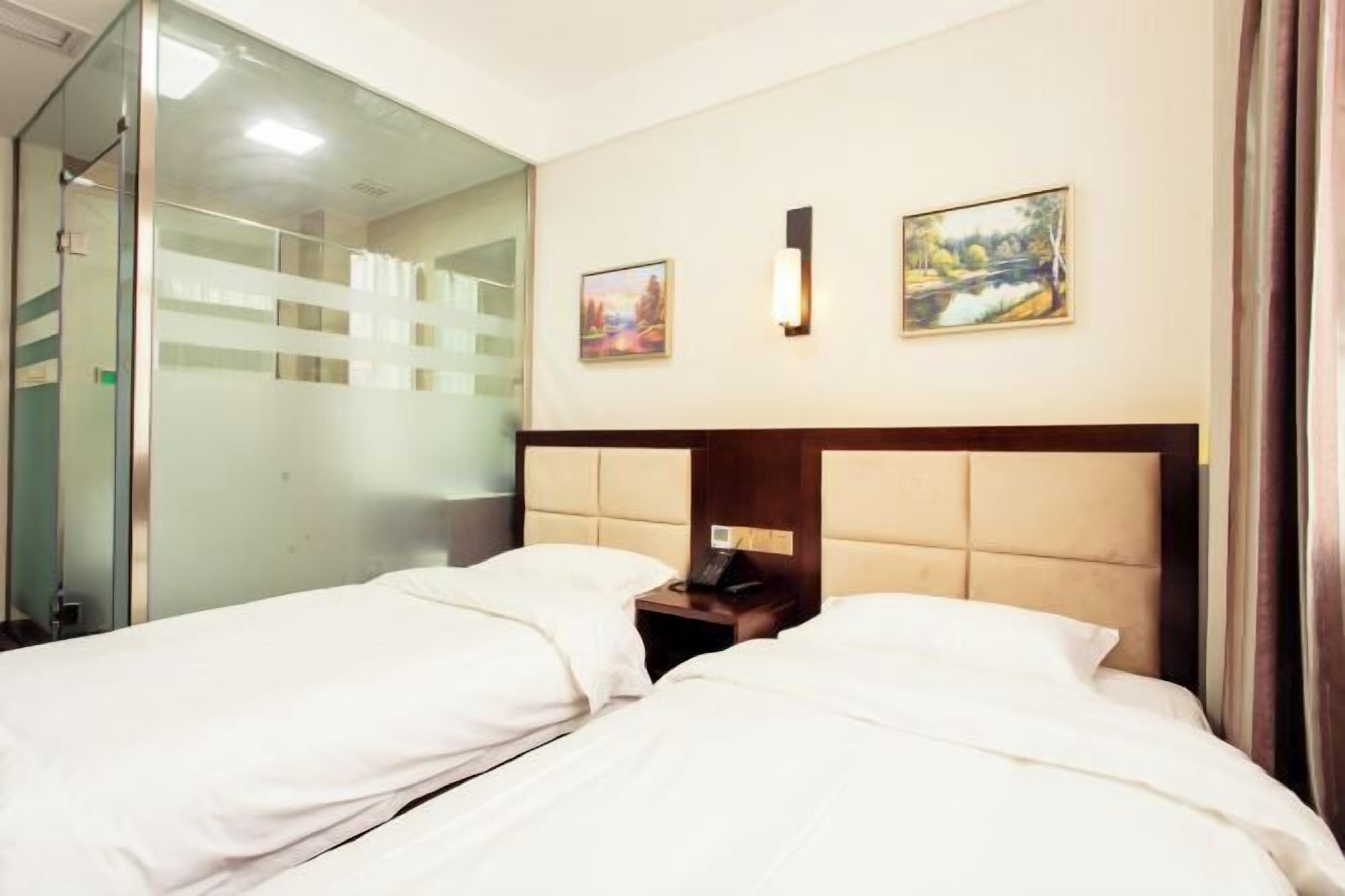 A hotel room with two beds, a glass partition, and two framed pictures on the wall.