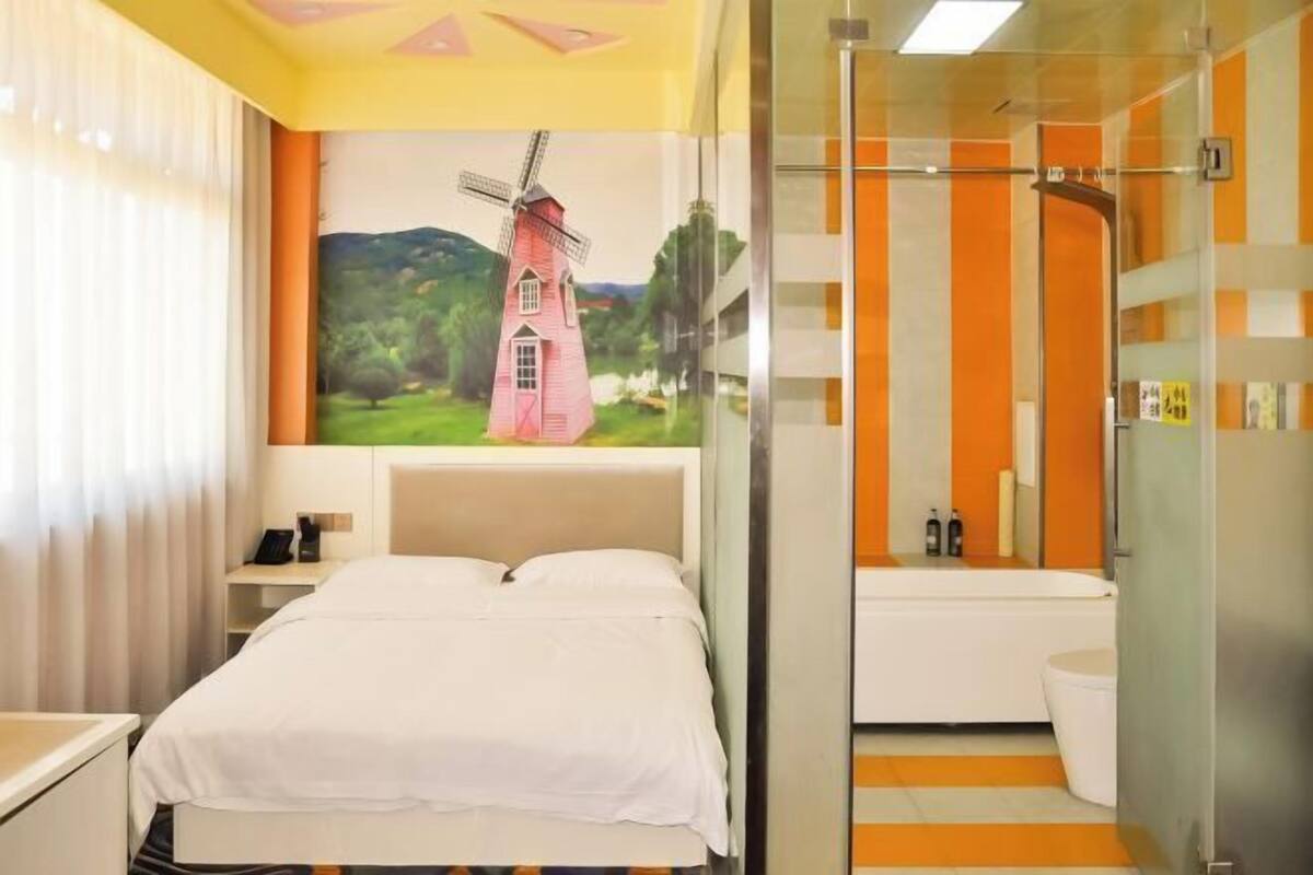 A hotel room with a bed, a bathroom with a bathtub, and a mural of a windmill.