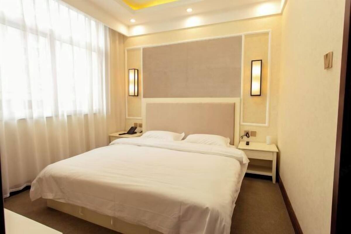 A hotel room with a large bed, bedside tables, a nightstand, and a window with curtains.