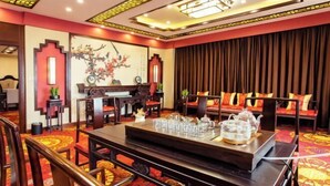 A traditional Chinese-style room with a red and gold carpet, wooden furniture, and a large painting on the wall.
