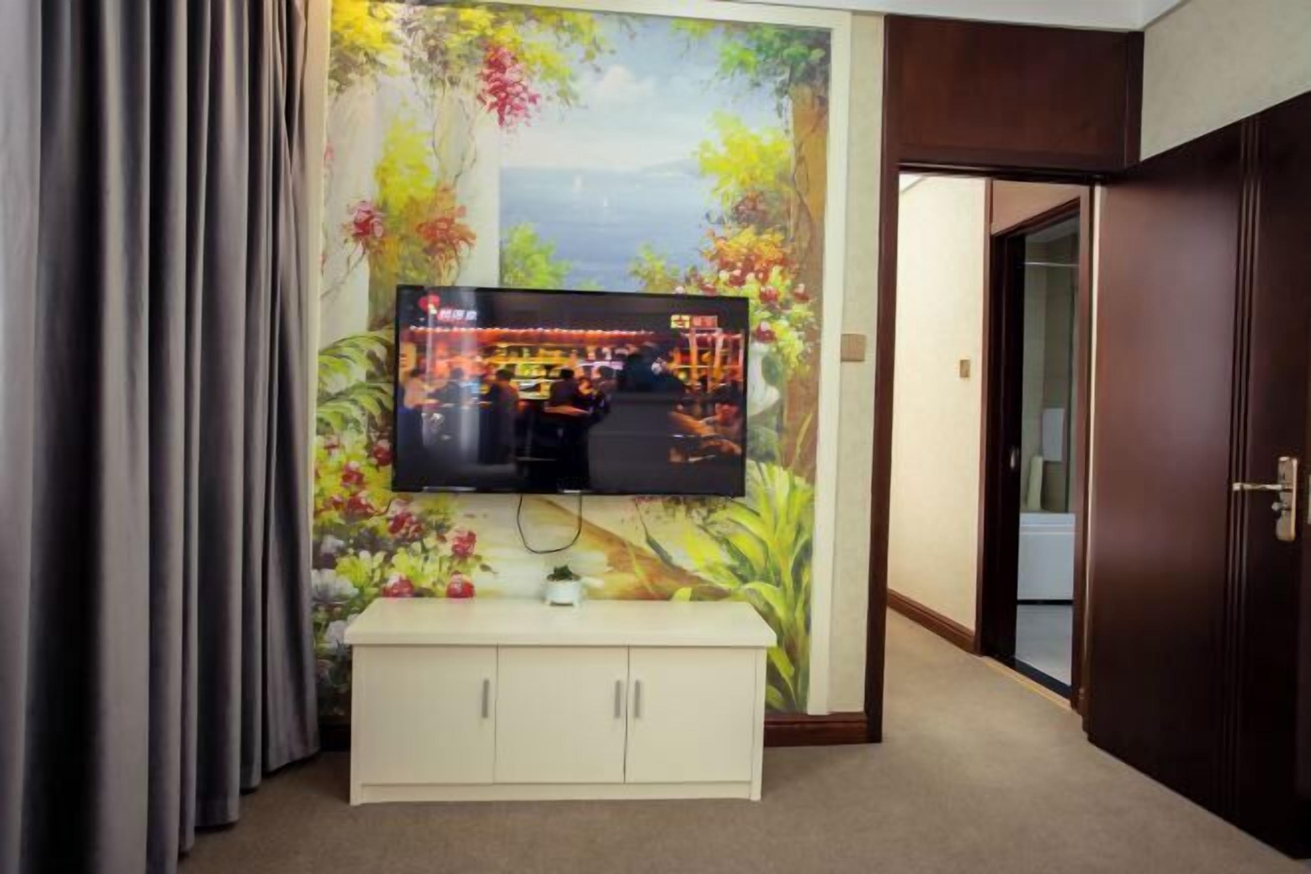 A television mounted on a wall with a floral mural, a white cabinet below, and a door to the right.