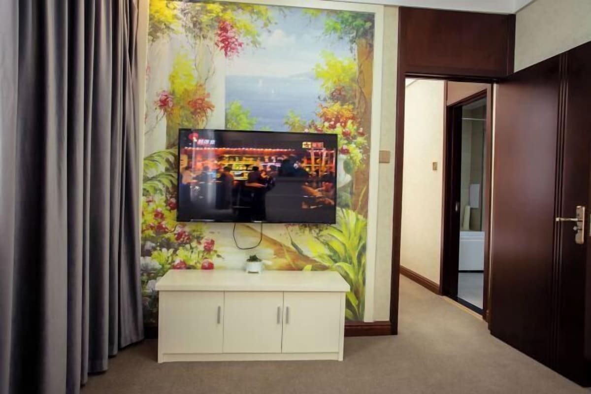 Un téléviseur fixé au mur, avec une fresque florale en arrière-plan, un meuble blanc en dessous et une porte sur la droite.