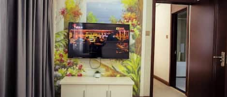 A television mounted on a wall with a floral mural, a white cabinet below, and a door to the right.