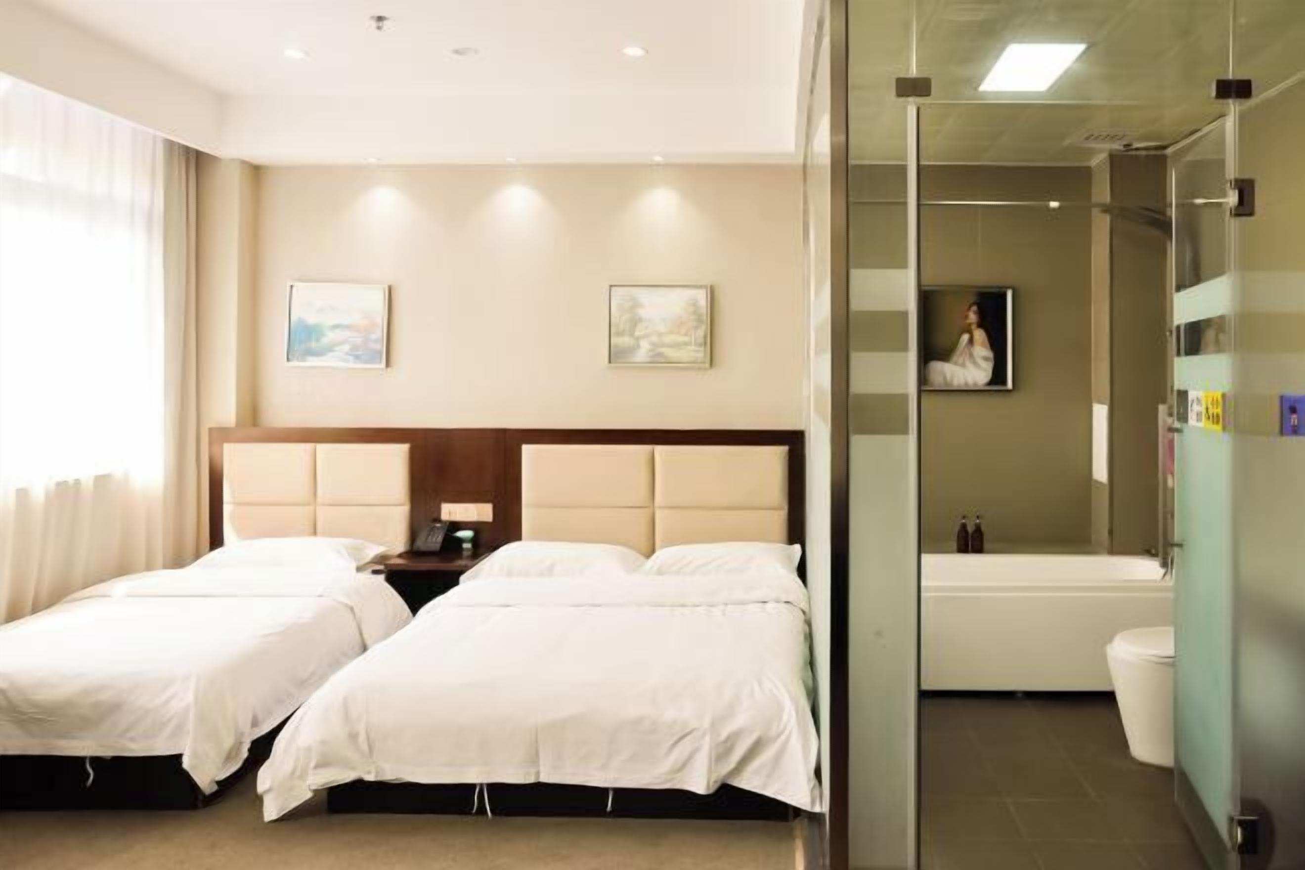 Hotellihuone, jossa on kaksi sänkyä, kylpyhuone ja lasiseinä.