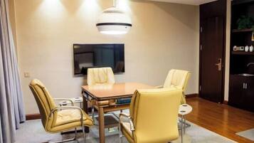 A modern dining area with a table and four chairs, a television mounted on the wall, and a kitchen area with cabinets and a refrigerator.