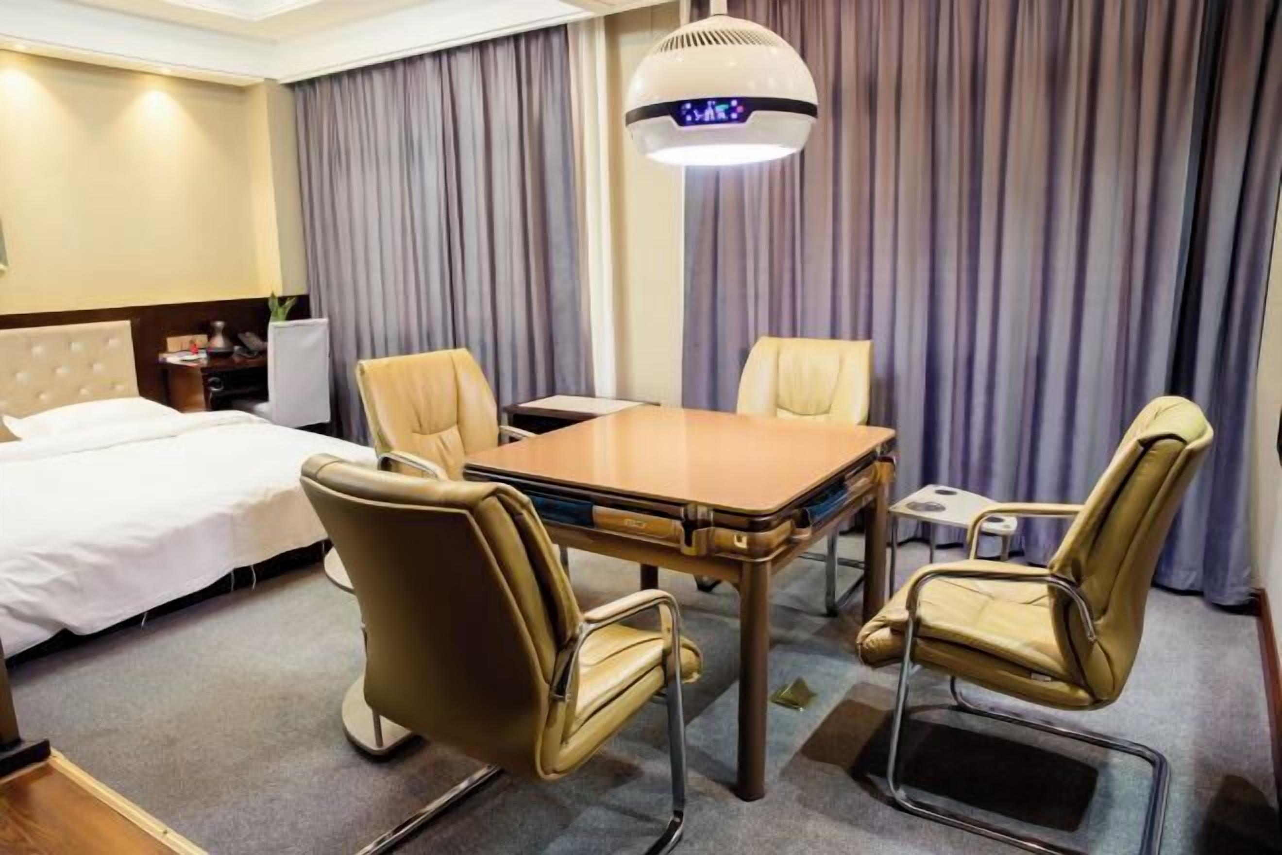 Une chambre d’h ôtel avec un lit, un bureau, deux chaises, une table et une grande fenêtre avec des rideaux.