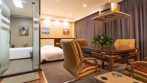 A hotel room with a bed, a desk, a chair, a table, and a plant.