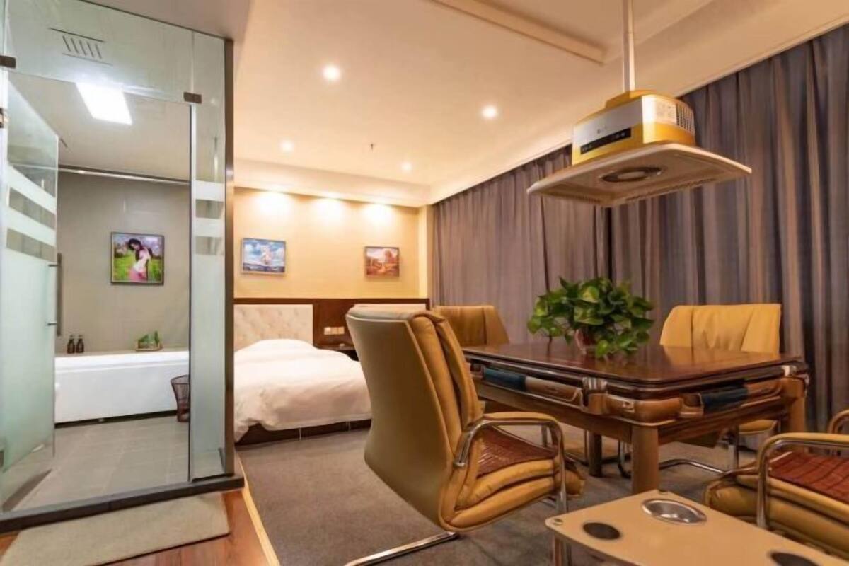 A hotel room with a bed, a desk, a chair, a table, and a plant.