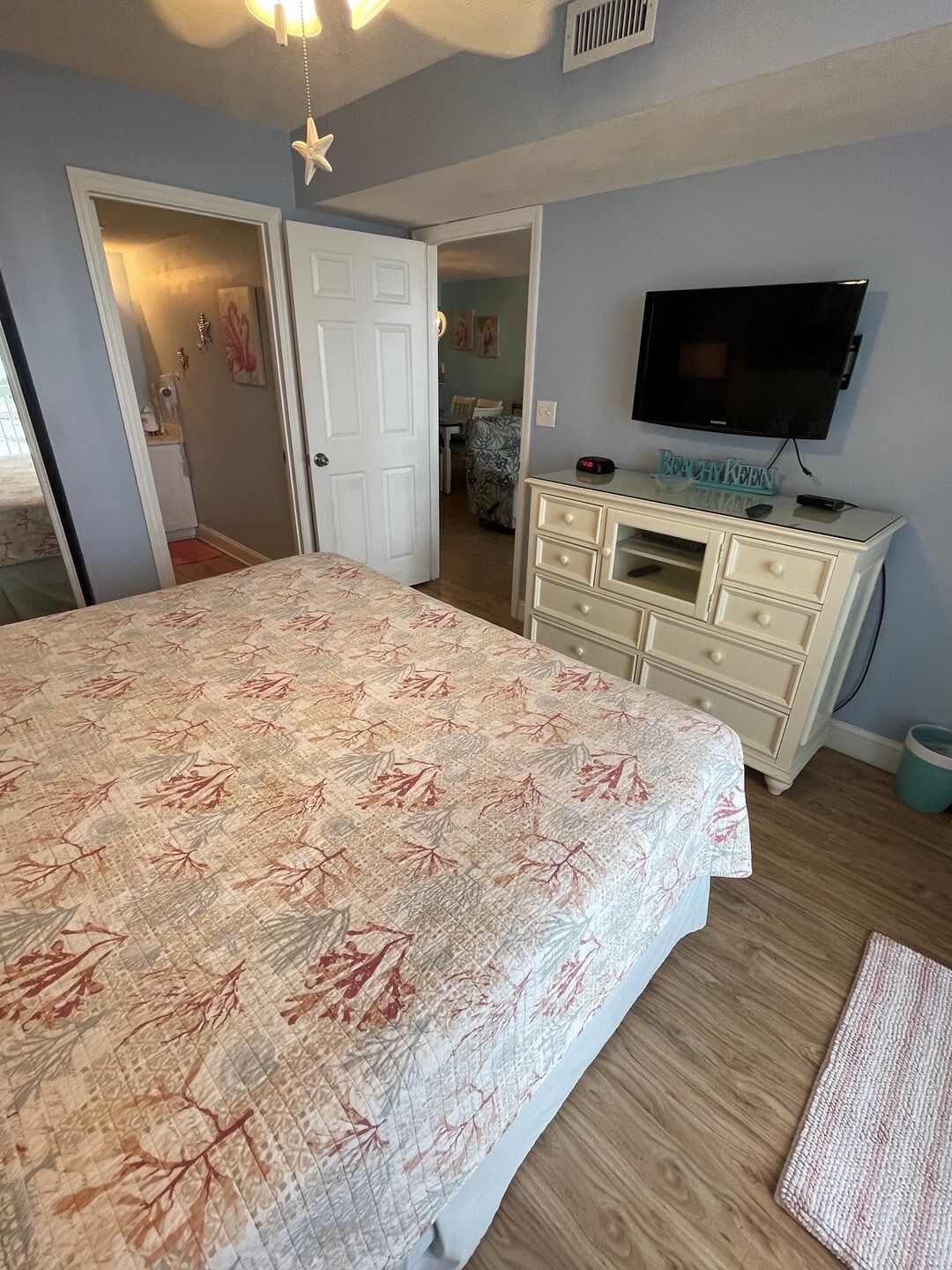 A bedroom with a bed, dresser, TV, and a star decoration on the ceiling.