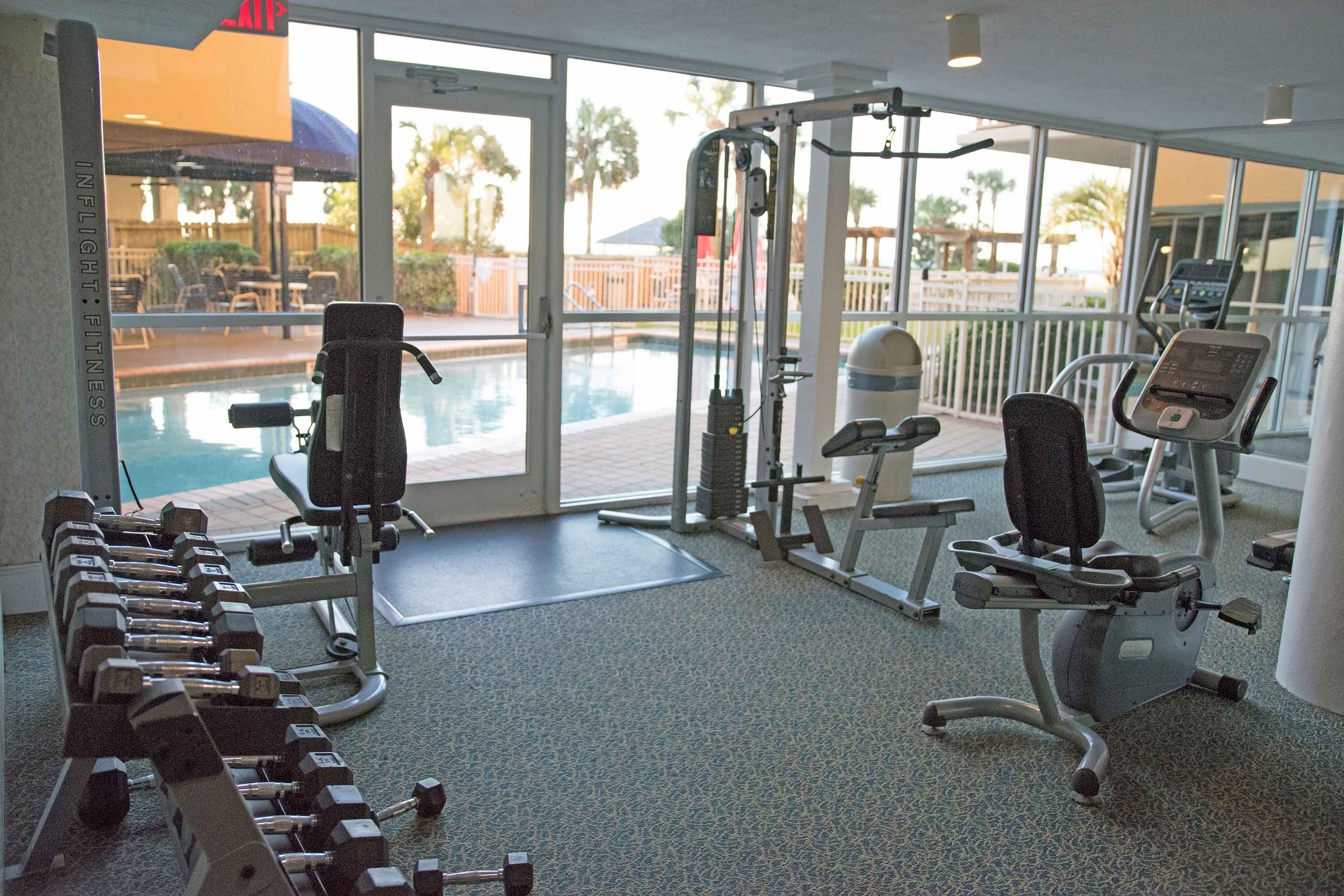 Una palestra con attrezzature per esercizi, una piscina e vista su palme.