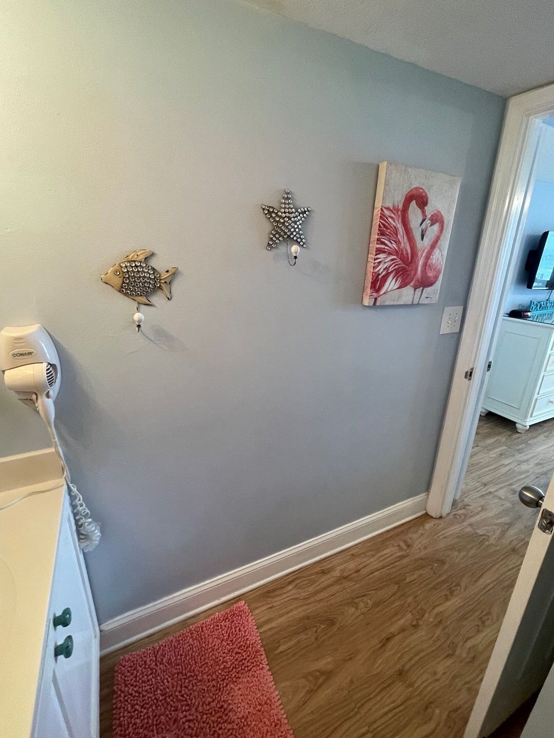 Un pasillo con una pared gris, un radiador blanco, un tapete rojo y un cuadro de flamencos.