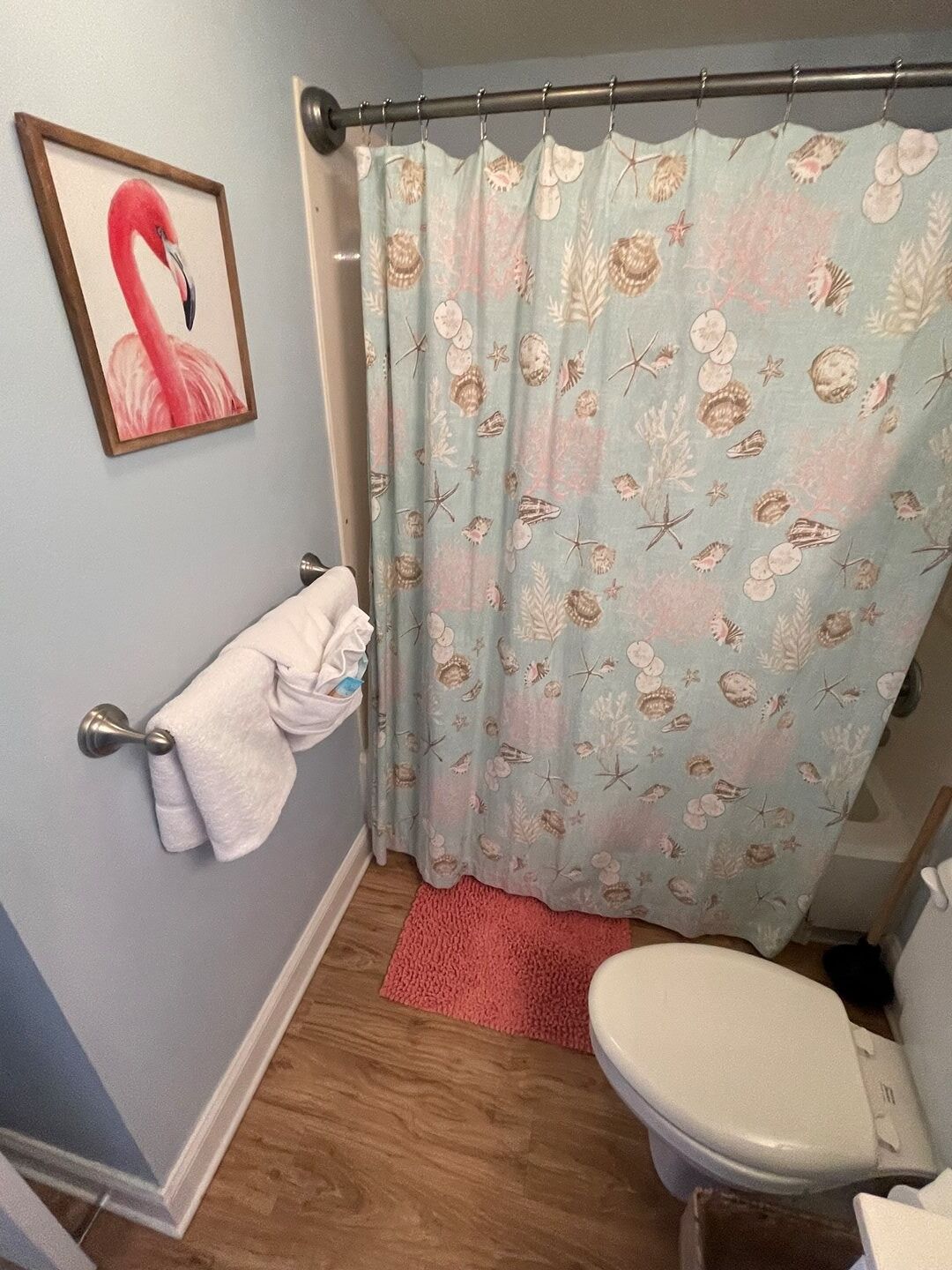 A bathroom with a shower curtain featuring a sea shell pattern, a white toilet, and a framed flamingo picture on the wall.