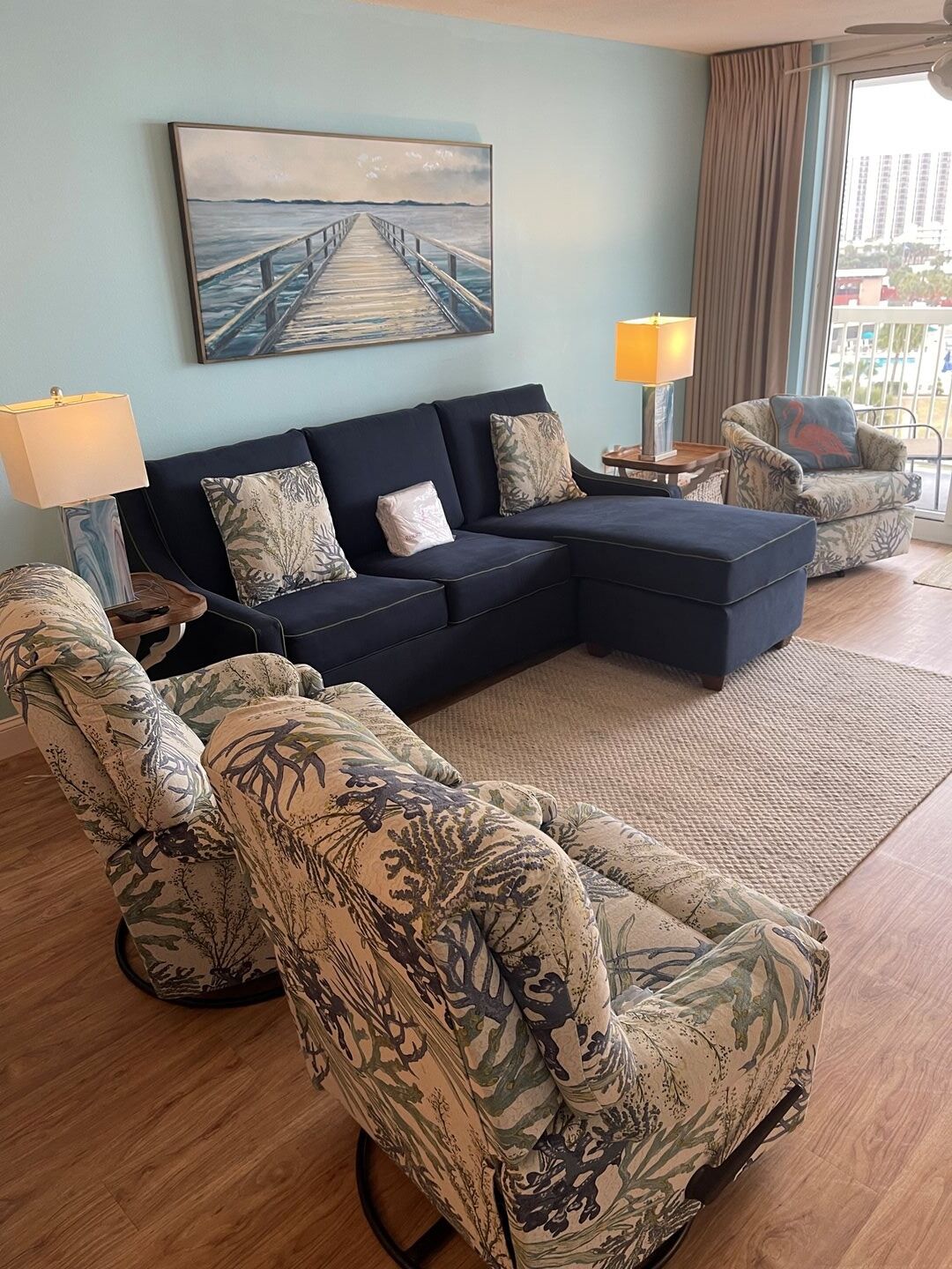 Ein Wohnzimmer mit einem dunkelblauen Sofa, gemusterten Sesseln, einem Couchtisch und einem Bild von einem Steg.