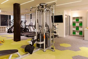 Un gimnasio con cintas de correr, máquinas de cable y una televisión montada en la pared.