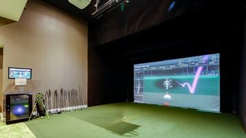 Ein Raum mit einem großen Bildschirm, der eine Golfsimulation zeigt, einem Projektor und einer Golfbag.