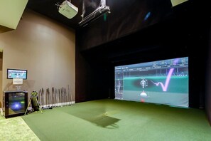 Una habitación con una pantalla grande mostrando una simulación de golf, un proyector y un bolso de golf.