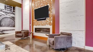 A modern interior with a flat-screen TV mounted on a textured wall, a fireplace, and two plush armchairs.