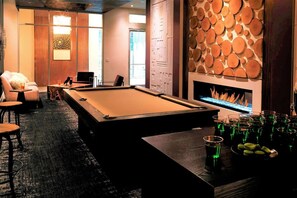 Una mesa de billar en una sala con chimenea, un sofá y una zona de bar con vasos.