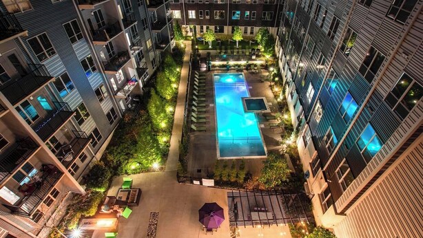 Um edifício residencial com vários andares, piscina no terraço, área de estar externa e um pátio bem iluminado.