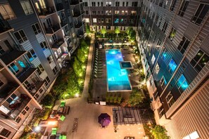 Zona de piscina en la azotea, rodeada de edificios residenciales con balcones y mobiliario de exterior.