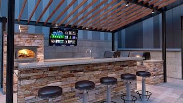 An outdoor bar area with a stone wall, wooden ceiling, and a flat-screen TV mounted above the bar.