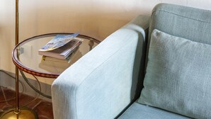 En ljusblå soffa med träben, placerad bredvid ett glasbord med en bok och en tidning på.