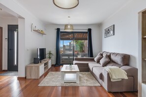 Ein modernes Wohnzimmer mit einer Couch, einem Couchtisch, einem Fernseher und einem Balkon mit Blick.