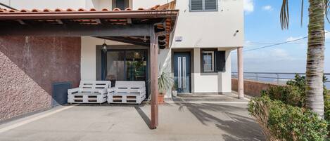 A modern building with a covered patio area, white walls, and a view of the sea.