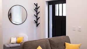 Una sala de estar moderna con un sofá gris, dos cojines amarillos, un espejo redondo y un perchero negro.