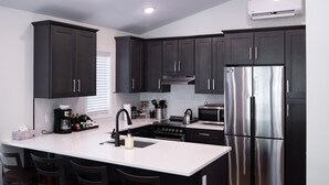 Una cocina moderna con armarios oscuros, un refrigerador de acero inoxidable, horno empotrado y encimera blanca.