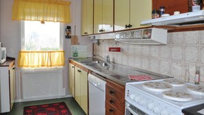 Una cocina con ventana, cortinas amarillas, estufa, pileta y alacenas.