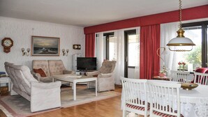 Una sala de estar con televisor, dos sillones, una mesa de centro y una mesa de comedor con sillas.