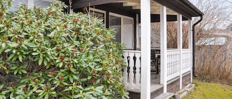 A house with a covered porch and a large bush in front.