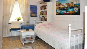 Un dormitorio con una cama individual, un escritorio con lámpara, una estantería y un cuadro de una escena portuaria.