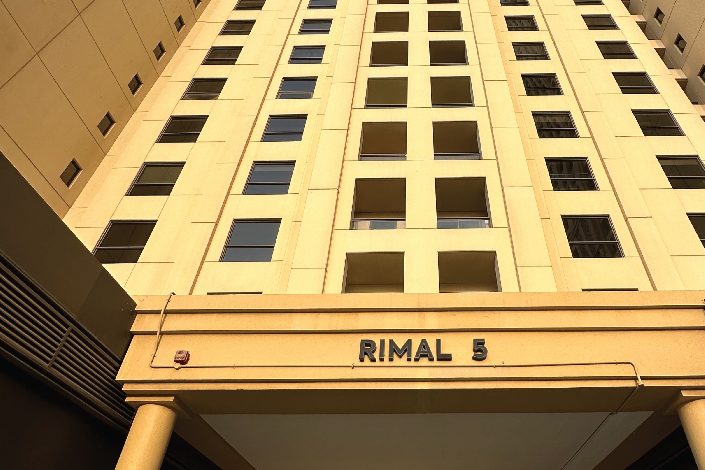 Um edifício alto com fachada bege e várias janelas. O edifício tem uma placa com a inscrição 