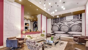 A modern living room with a sofa, coffee table, and chairs, a patterned rug, and a large wall mural. - 4th Street Suites - Splash King Bed Suite (Louisville)