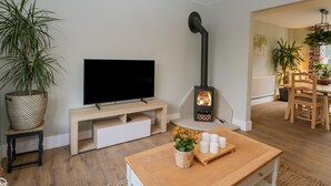 A living room with a TV, a wooden table with candles, and a black stove. - Birch House (Corsham)