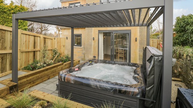 A hot tub under a pergola in a backyard with a wooden fence and a house in the background. - Birch House (Corsham)
