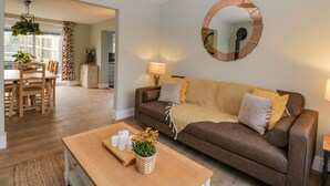 A modern living room with a brown leather sofa, a wooden coffee table, and a dining area with a wooden table and chairs. - Birch House (Corsham)
