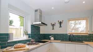 A kitchen with white cabinets, a black stove, and a window with blinds. - Birch House (Corsham)